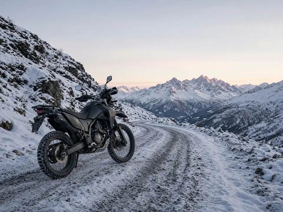 Dual-sport motorcycle parked on a snowy mountain road at dawn